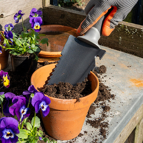 Mini wortelzaag schept potgrond in een terracotta bloempot met viooltjes