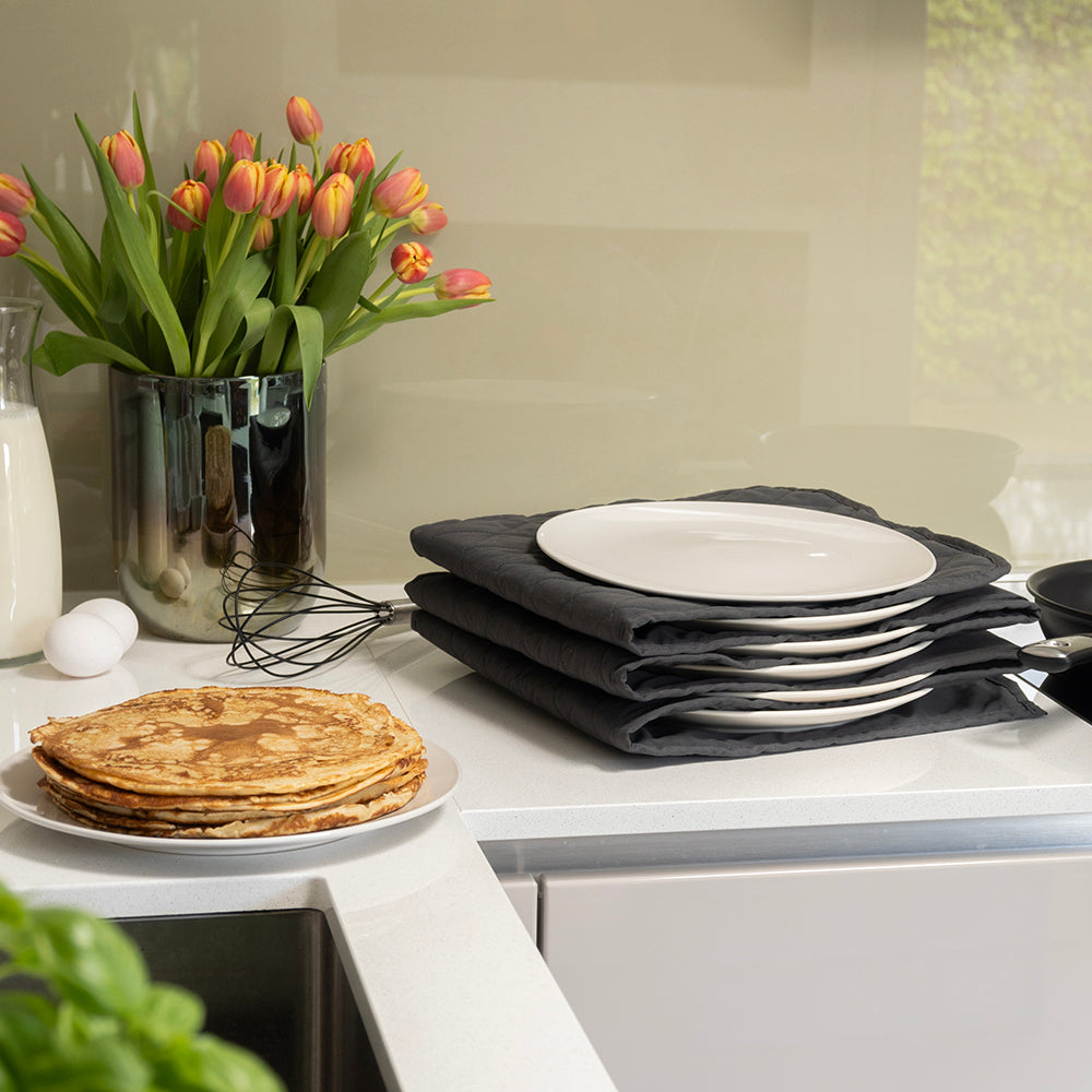 Elektrische bordenwarmer met borden op het aanrecht naast een stapel pannenkoeken en tulpen
