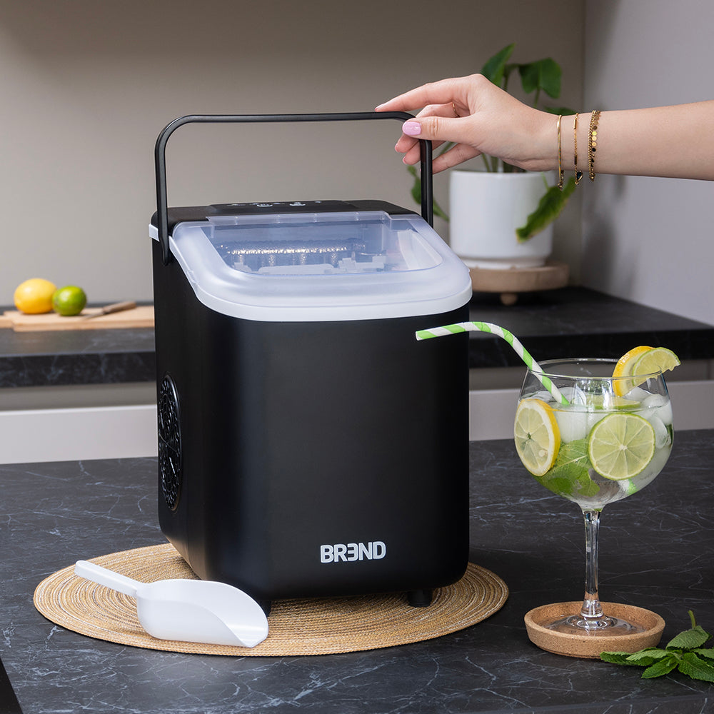 Hand tilt de zwarte ijsblokjesmachine op aan de draagbeugel, naast een glas met limoen