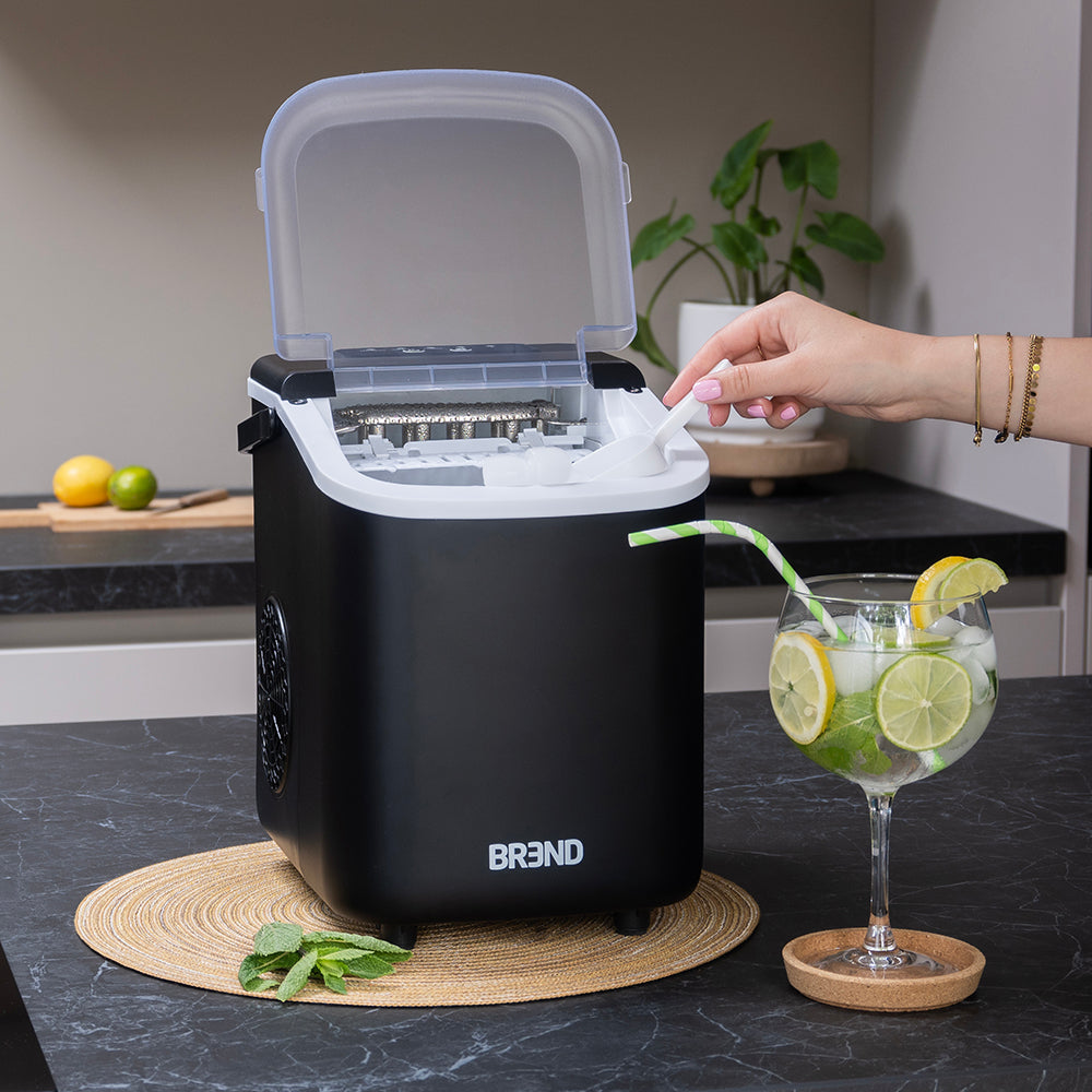 Hand pakt ijsblokjes uit de geopende zwarte ijsblokjesmachine op het aanrecht