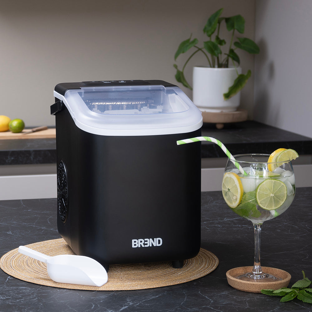 Zwarte ijsblokjesmachine op het aanrecht naast een cocktail met limoen en de ijsschep