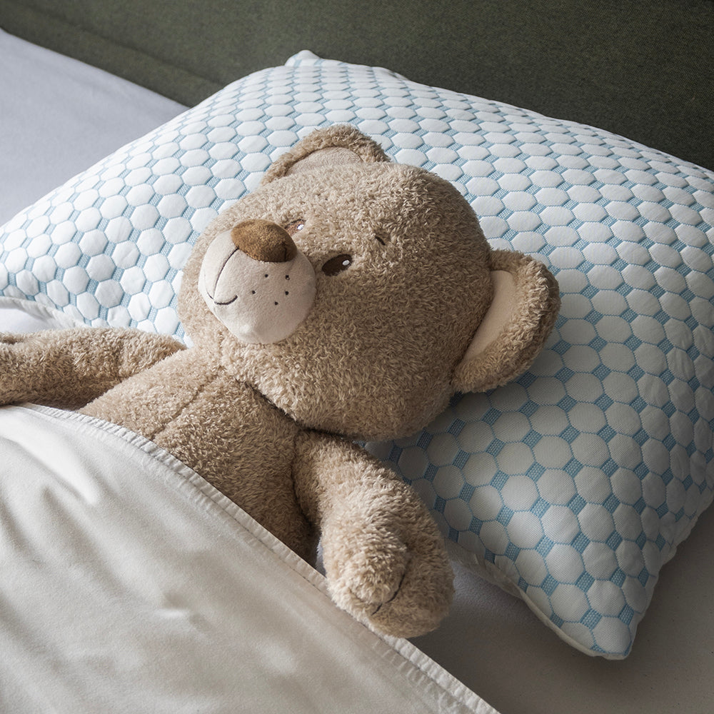 Knuffelbeer ligt met zijn hoofd op de blauwe verkoelende kant van het hoofdkussen