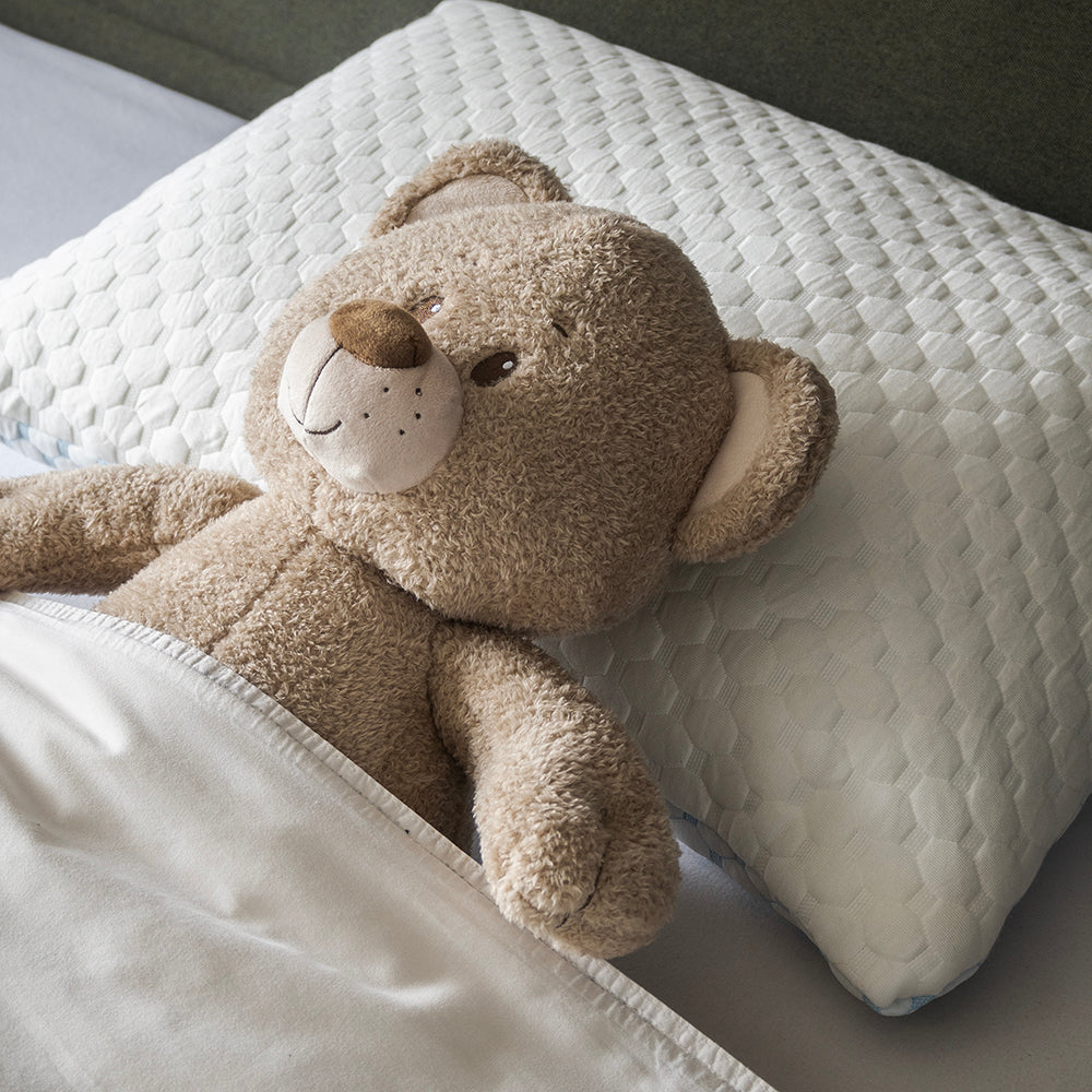 Knuffelbeer ligt op zijn rug op de witte kant van het hoofdkussen