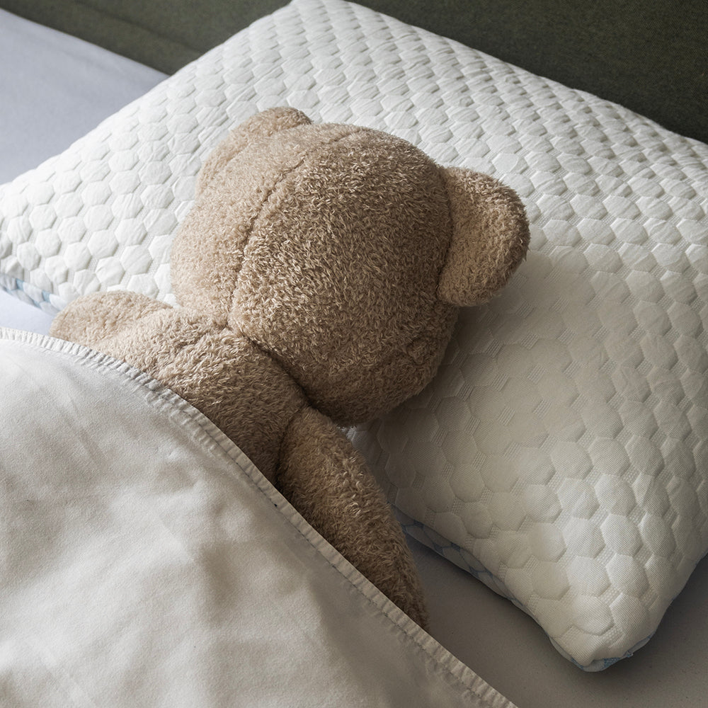 Knuffelbeer ligt op zijn zij op het witte hoofdkussen, van achteren gezien
