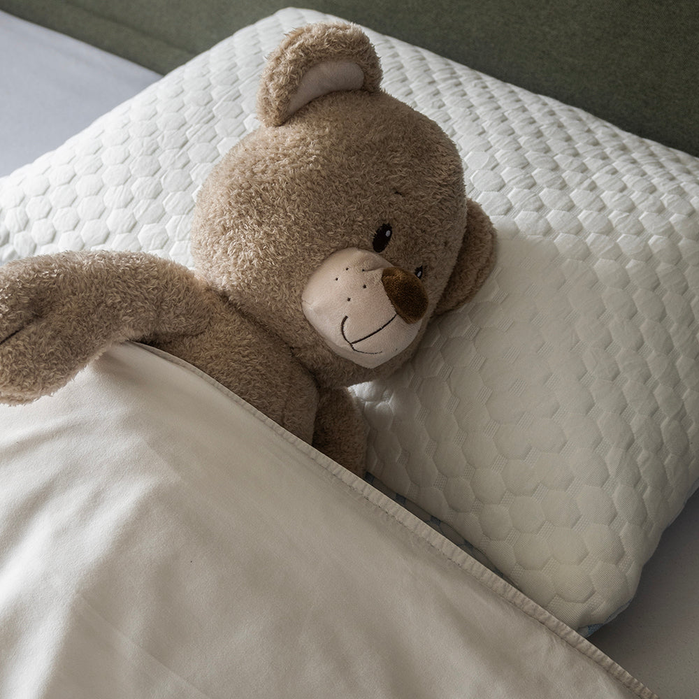 Knuffelbeer ligt onder het dekbed op het witte hoofdkussen