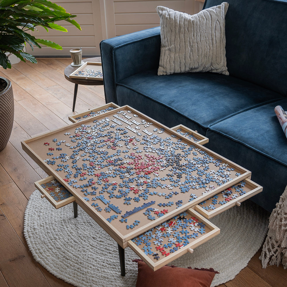 Houten puzzelplaat met uitgeschoven lades vol puzzelstukjes op een salontafel voor de bank