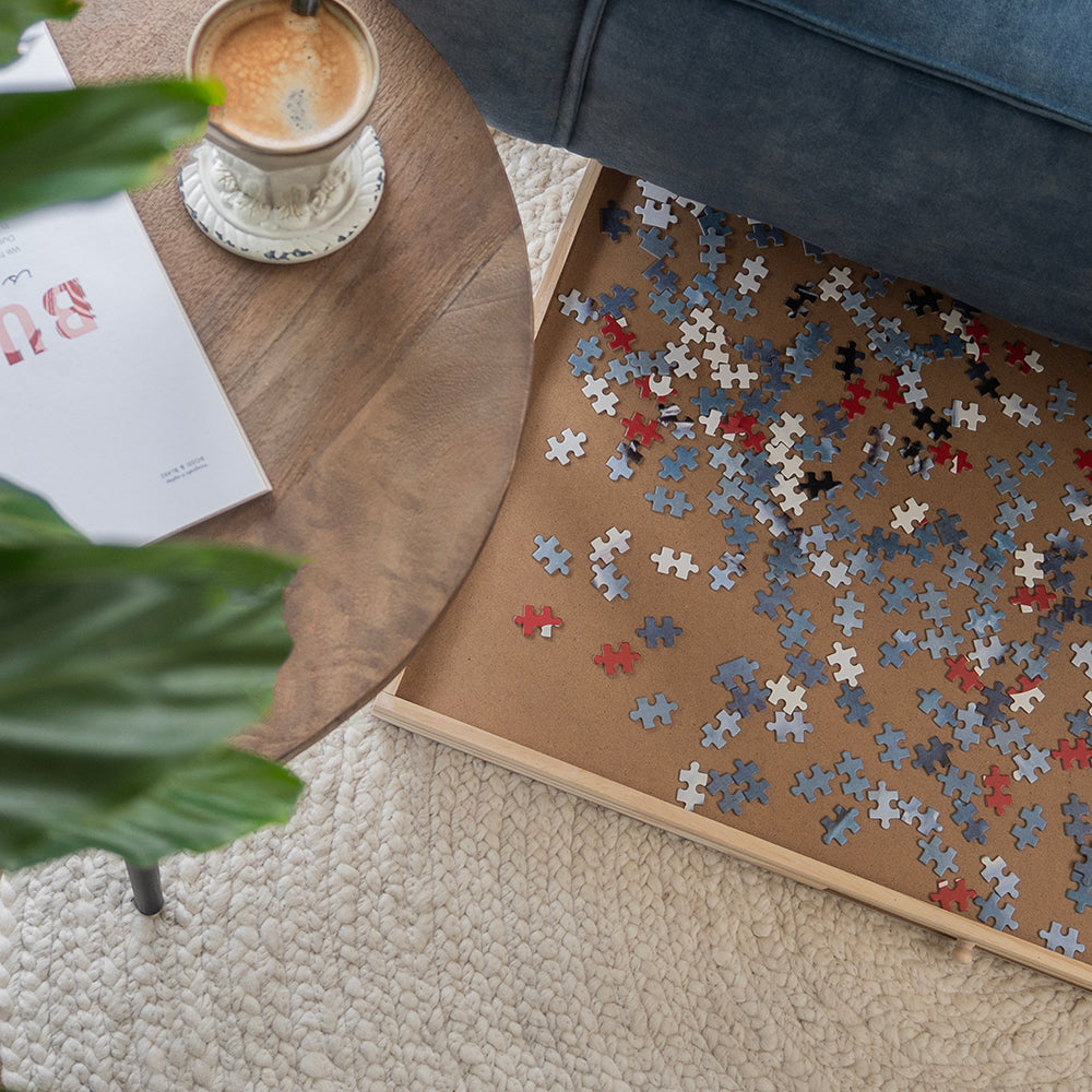 Grote puzzelplaat met losse puzzelstukjes op de vloer naast een bijzettafel met koffie