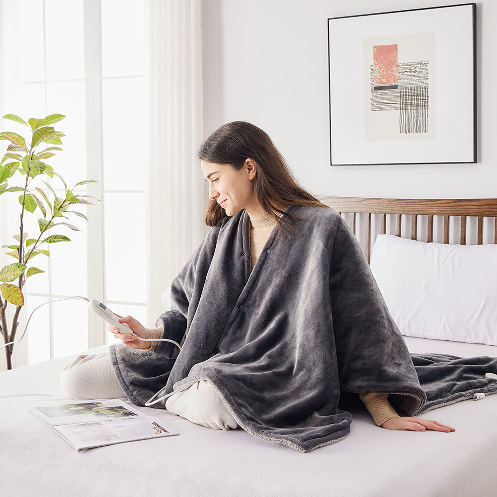 Vrouw zit op bed in de elektrische poncho en stelt de warmte in met de bediening
