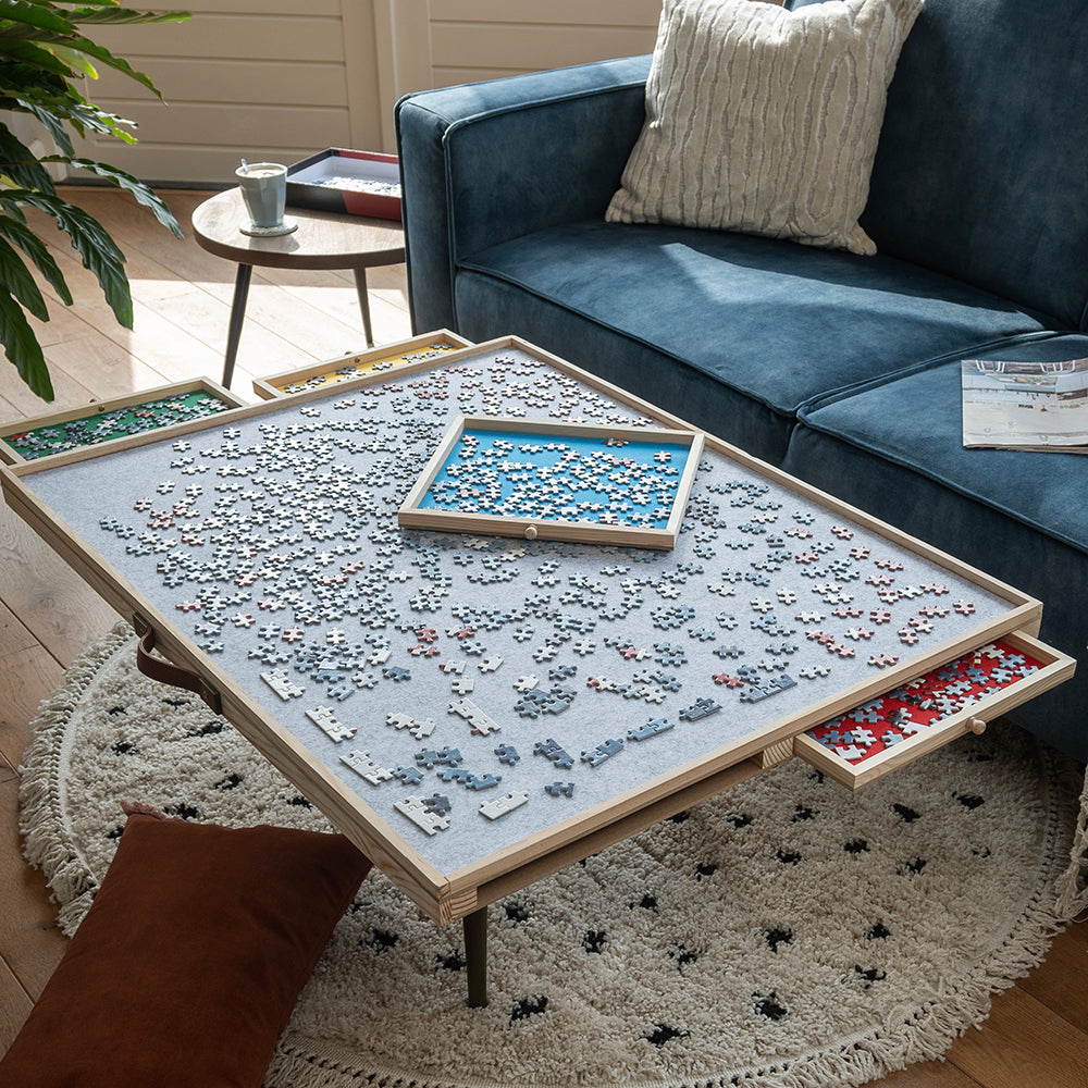Verstelbare puzzelplaat op een salontafel met uitgeschoven vilten lades en een lade boven op de puzzel