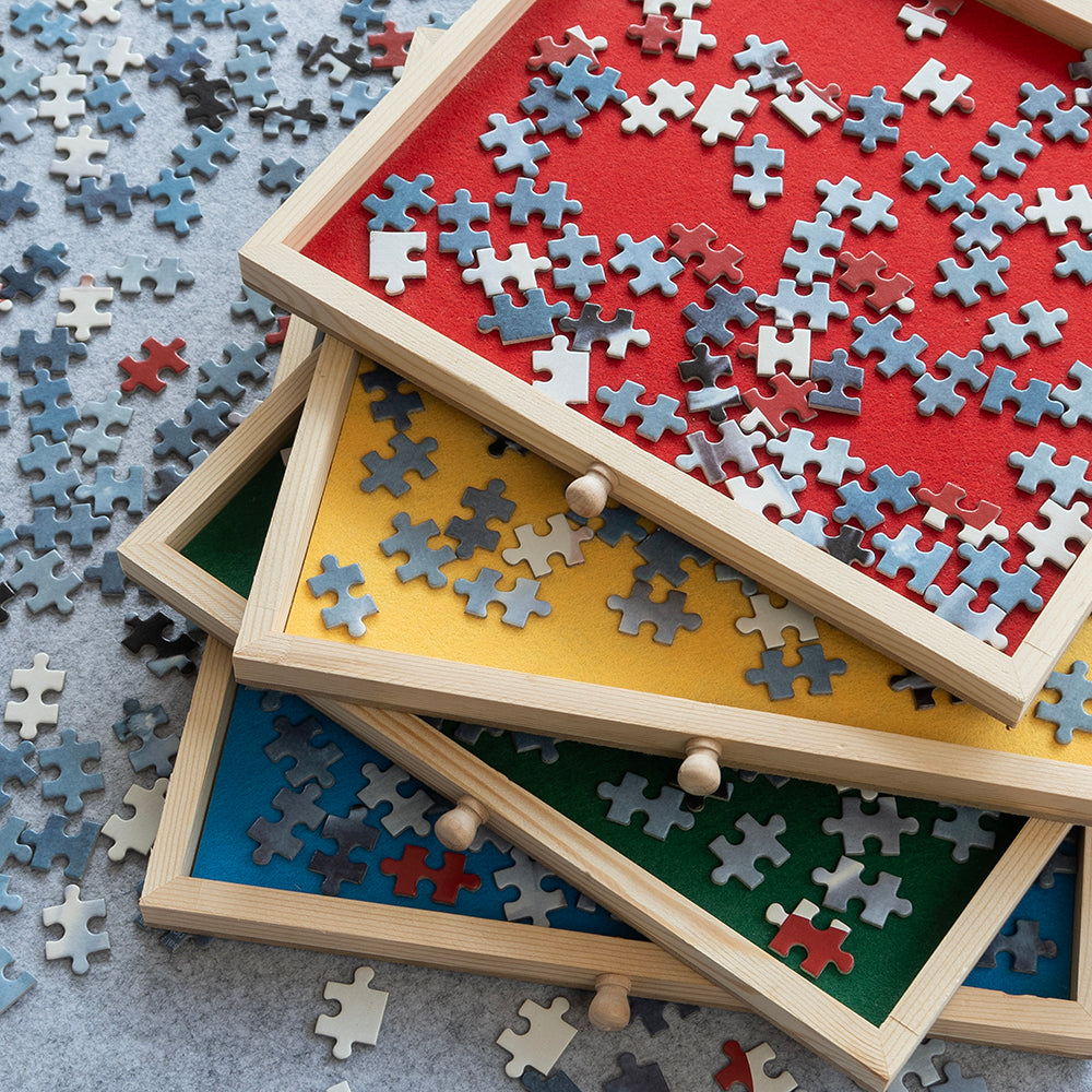 Vier lades met rood, geel, groen en blauw vilt gestapeld, met gesorteerde puzzelstukjes