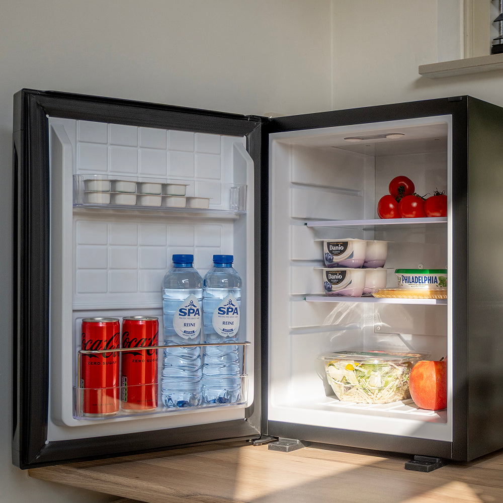 Geopende mini koelkast gevuld met blikjes, flessen water en etenswaren