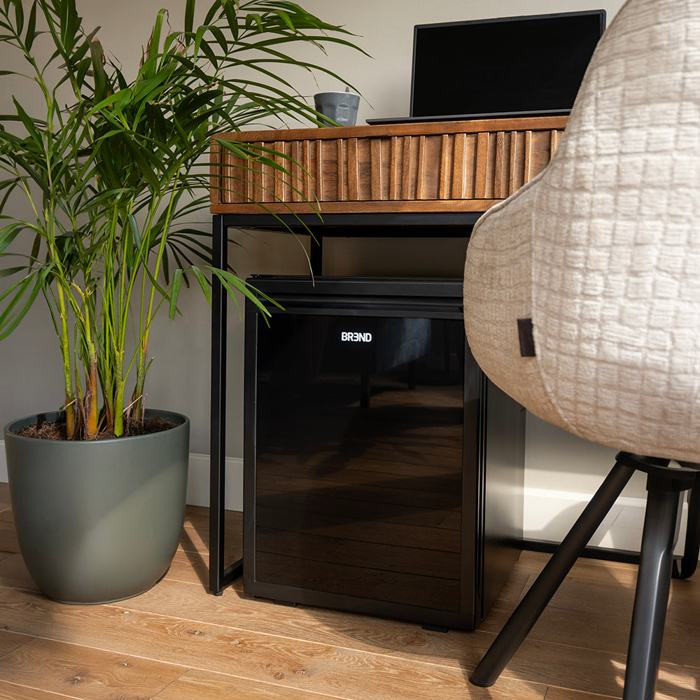 Zwarte mini koelkast staat onder een bureau in een thuiskantoor