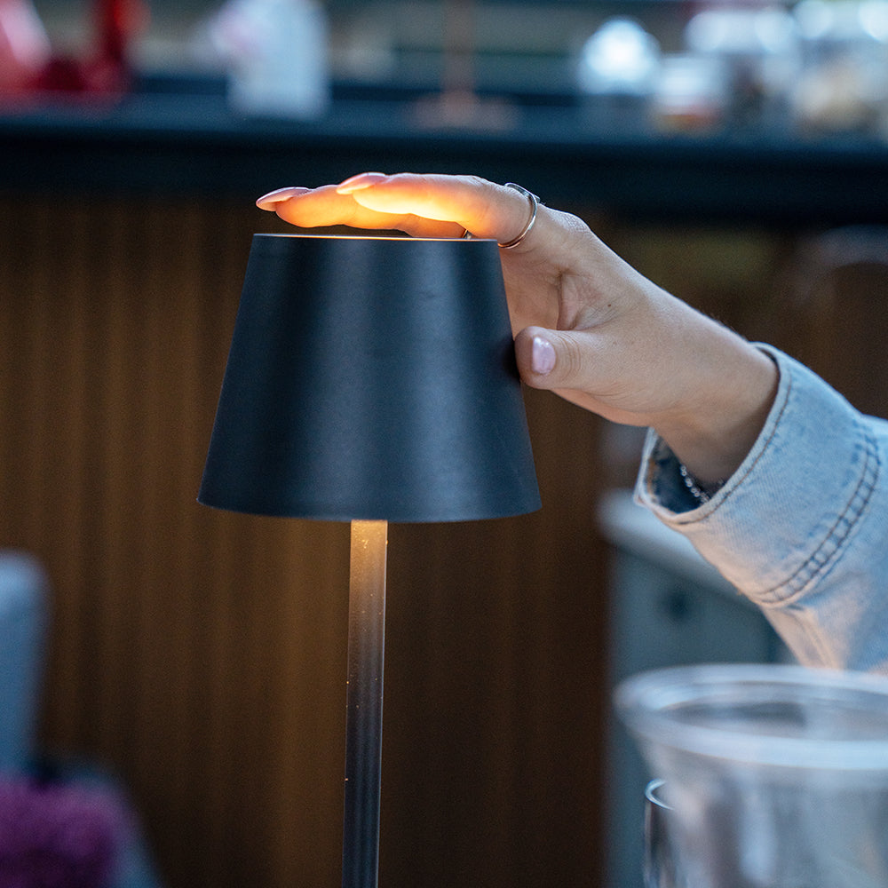 Hand raakt de bovenkant van de zwarte tafellamp aan om het licht te bedienen