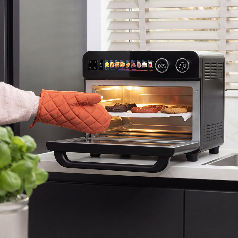 Hand met oranje ovenhandschoen haalt een bakplaat met koekjes uit de Combi Airfryer Oven