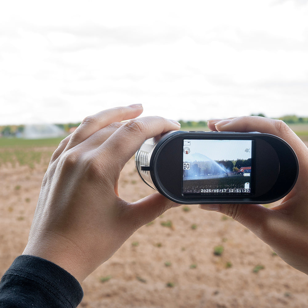 Twee handen houden de digitale verrekijker vast, het scherm toont een landschap