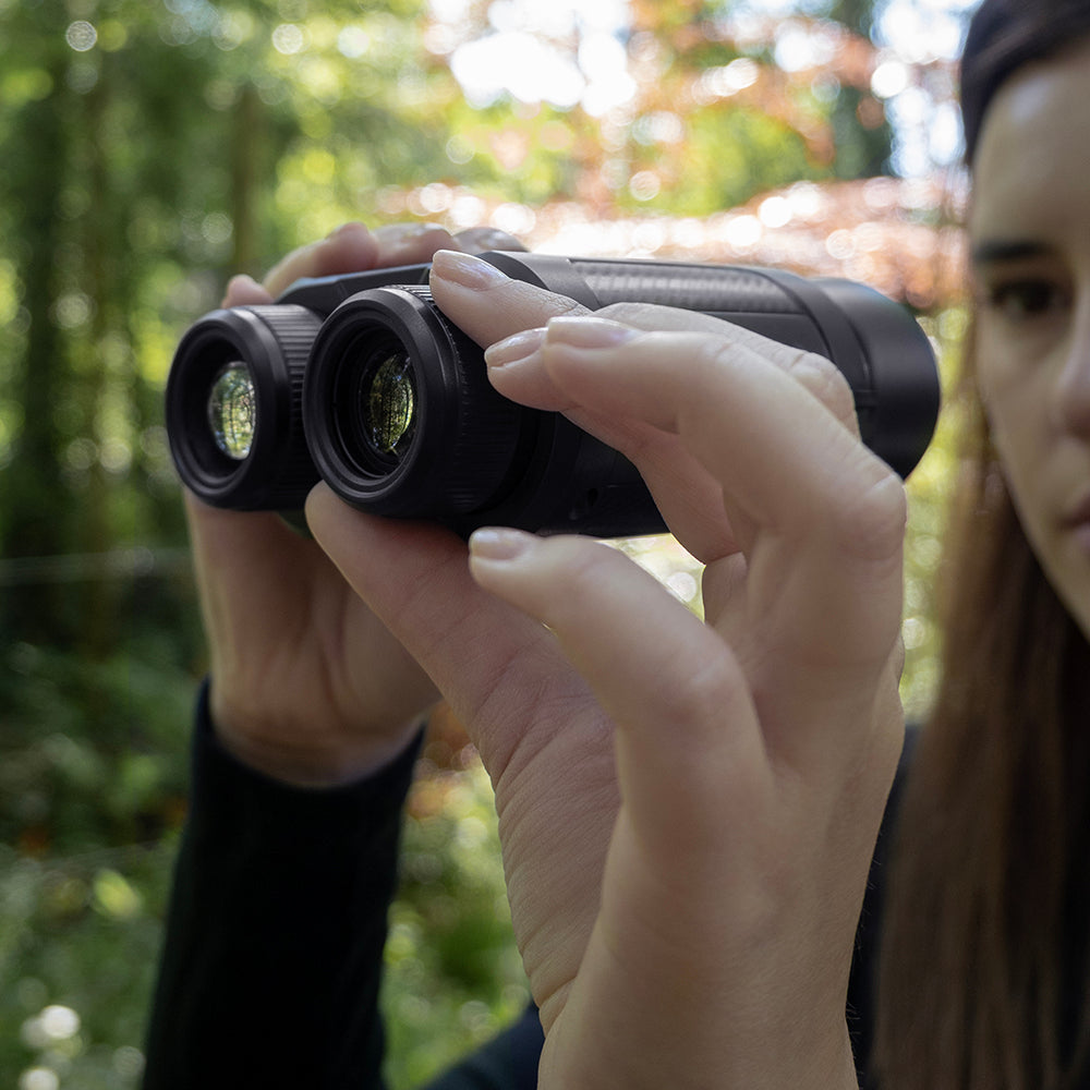 Vrouw stelt de digitale verrekijker scherp in het bos