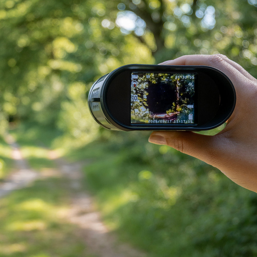 Hand houdt de digitale verrekijker vast op een bospad, het scherm toont de omgeving