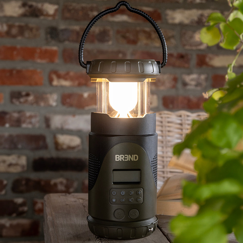 Noodradio met brandende lantaarn op een tuintafel voor een bakstenen muur