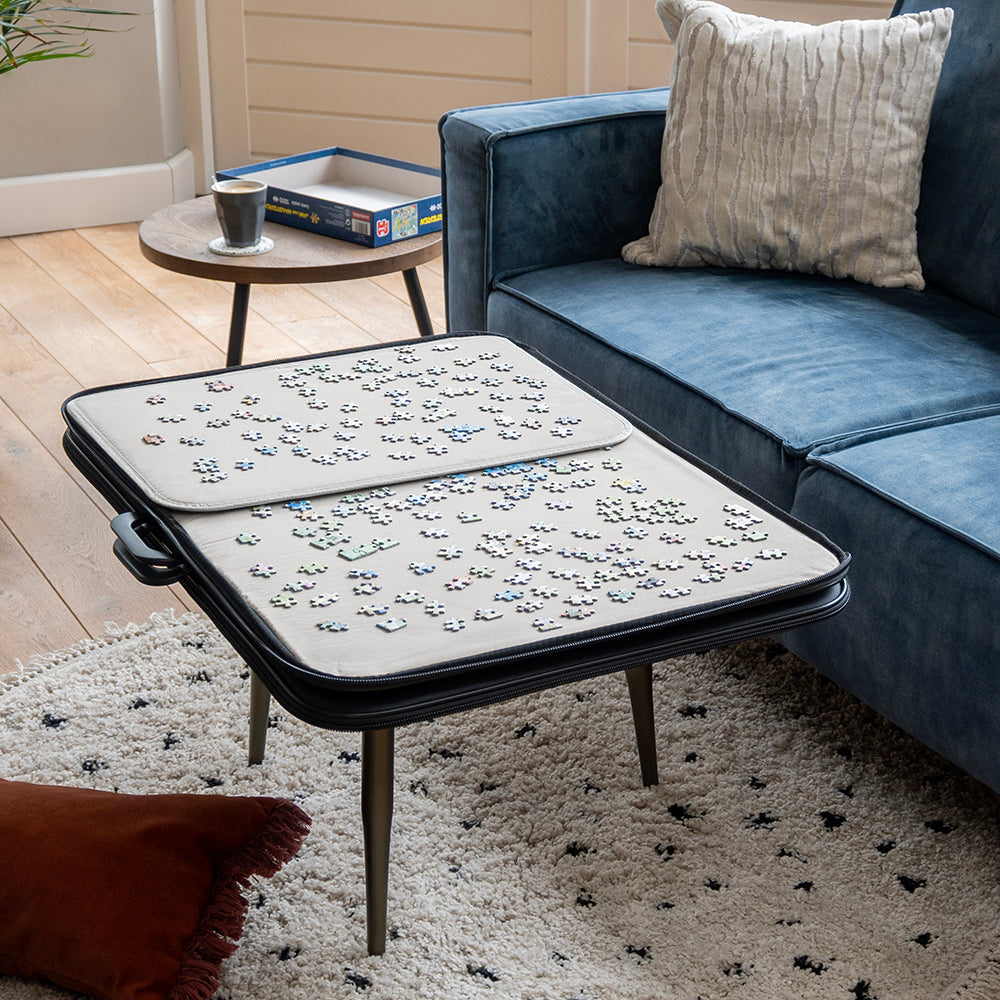 Geopende puzzelmap op een salontafel met twee sorteerbladen vol puzzelstukjes