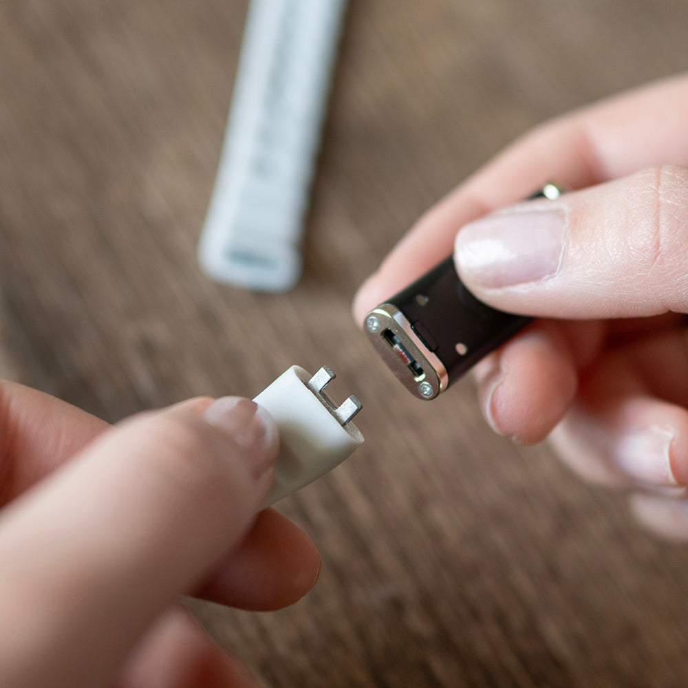 Handen houden de losse activity tracker en de magnetische oplader bij elkaar