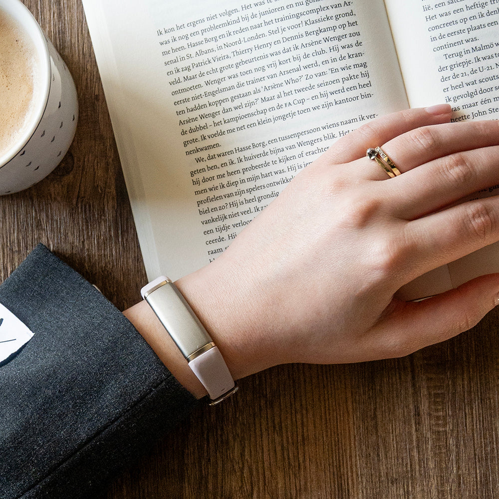 Roze activity tracker om de pols van iemand die een boek leest met een kop koffie ernaast