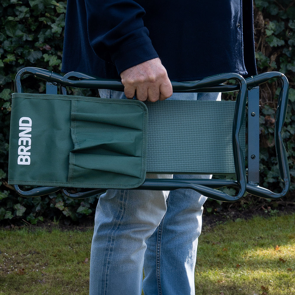Man draagt de ingeklapte tuinkruk in één hand door de tuin