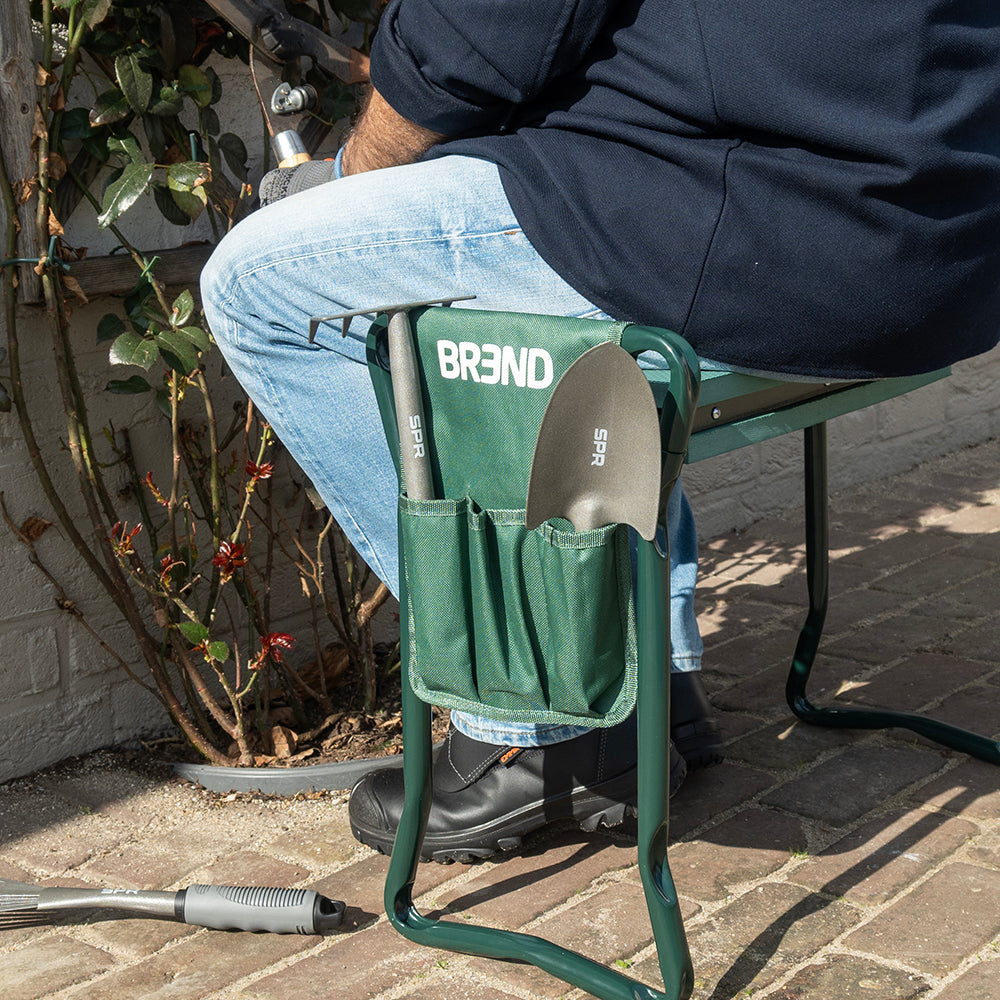Man zit op de tuinkruk met een schepje in de gereedschapstas naast zich