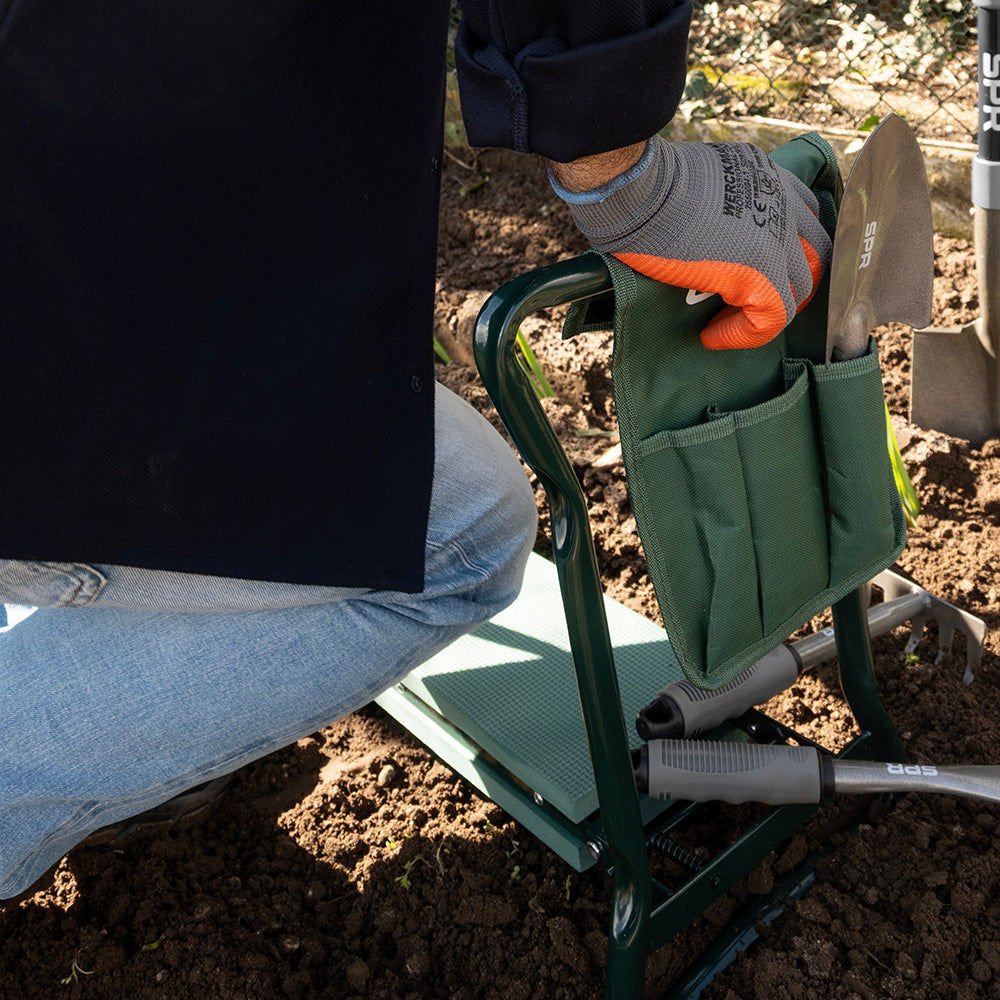 Man knielt in de moestuin en pakt gereedschap uit de tas van de tuinkruk