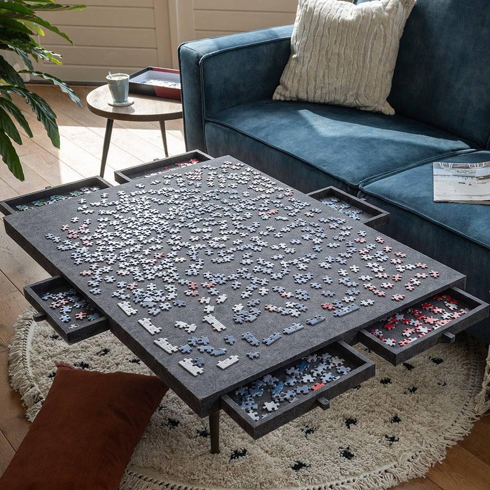 Grote vilten puzzelplaat op een salontafel met uitgeschoven lades vol puzzelstukjes