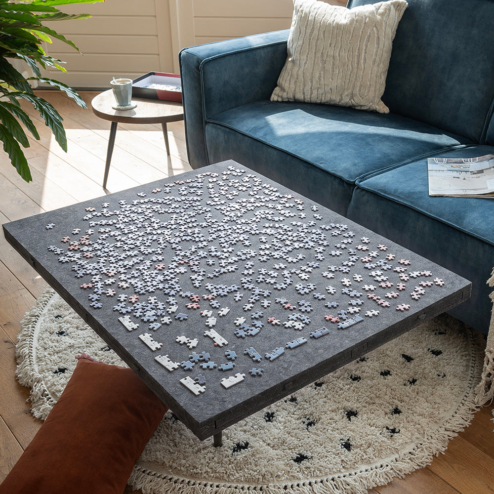 Grote vilten puzzelplaat met puzzelstukjes op een salontafel, de lades gesloten